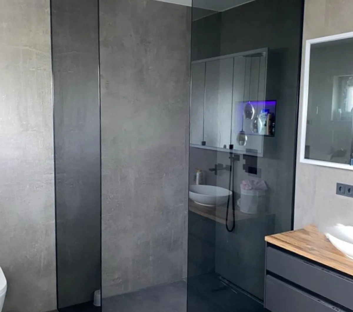 Walk-in-Glasdusche mit schwarzer Armatur in einem Bad mit Betonoptik-Fliesen und Holzwaschtisch, Kaiserslautern