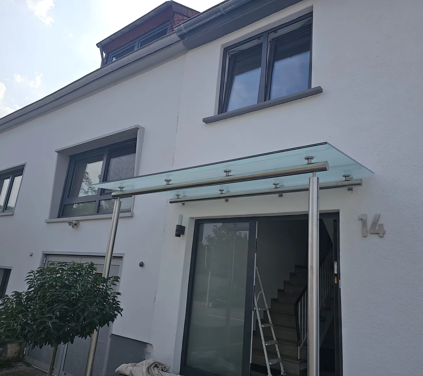 Glasvordach über einer Haustür mit Edelstahlhaltern an weißer Fassade, Zweibrücken